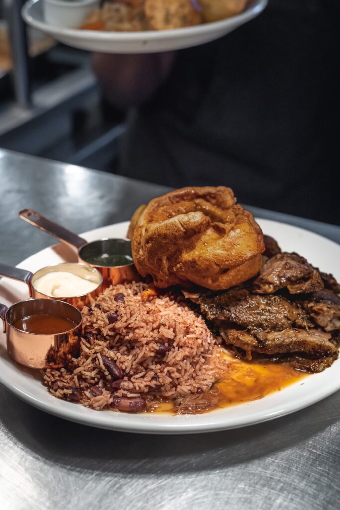 A plate of Caribbean-style rice and beans, served with meat, a Yorkshire pudding, and sauces in copper cups.