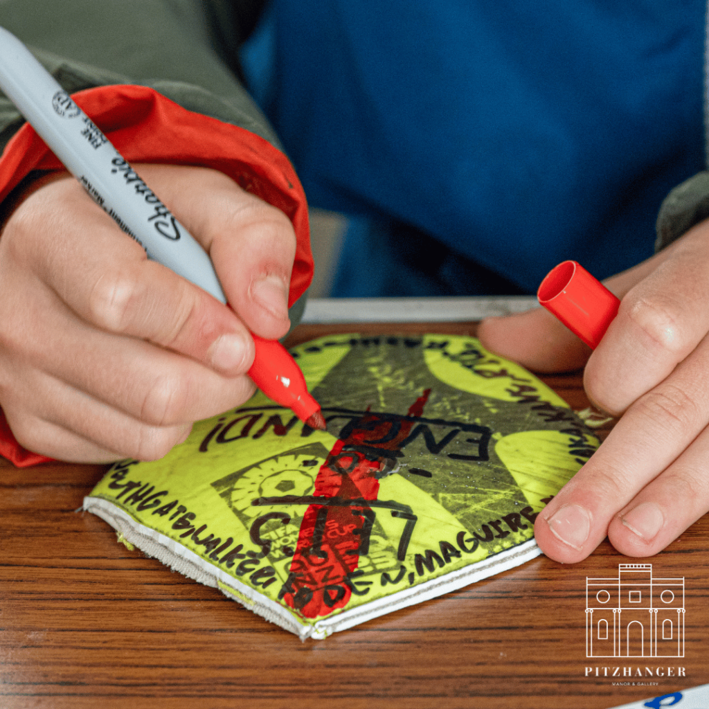 Close-up of a child using a red marker to add details on a patch for the collaborative sculpture project.