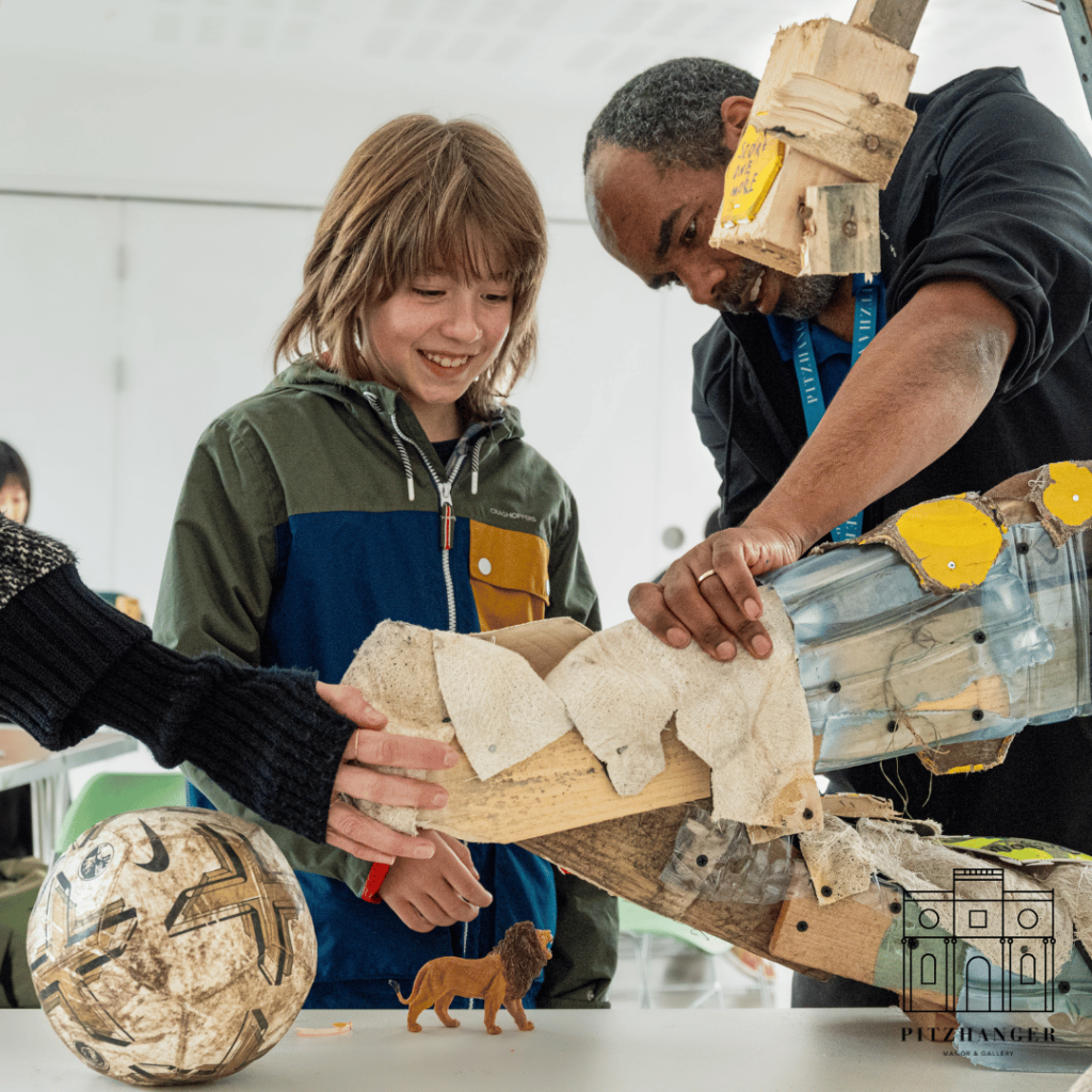 Children and a facilitator work together, adding elements to a lion sculpture during a community art workshop.