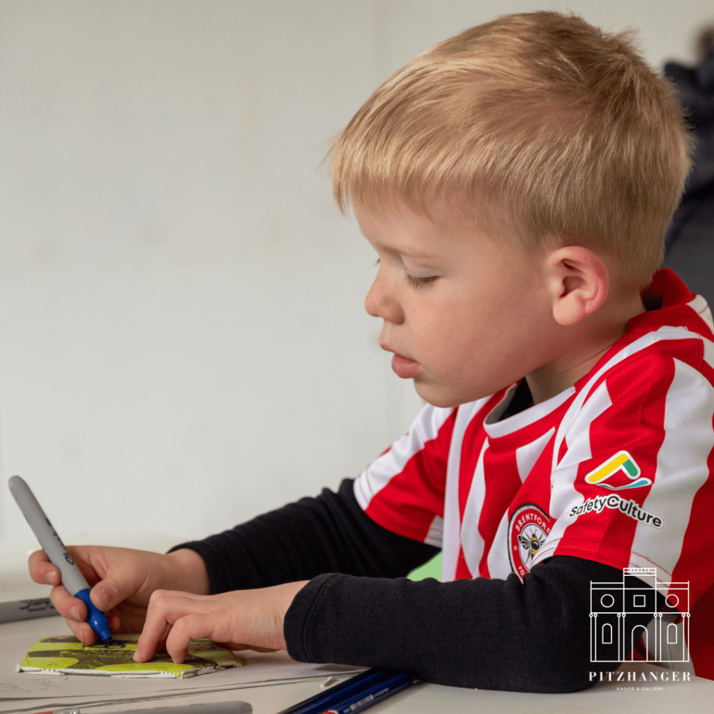 A focused child in a red jacket adds colorful designs to a piece of patchwork for the lion sculpture.