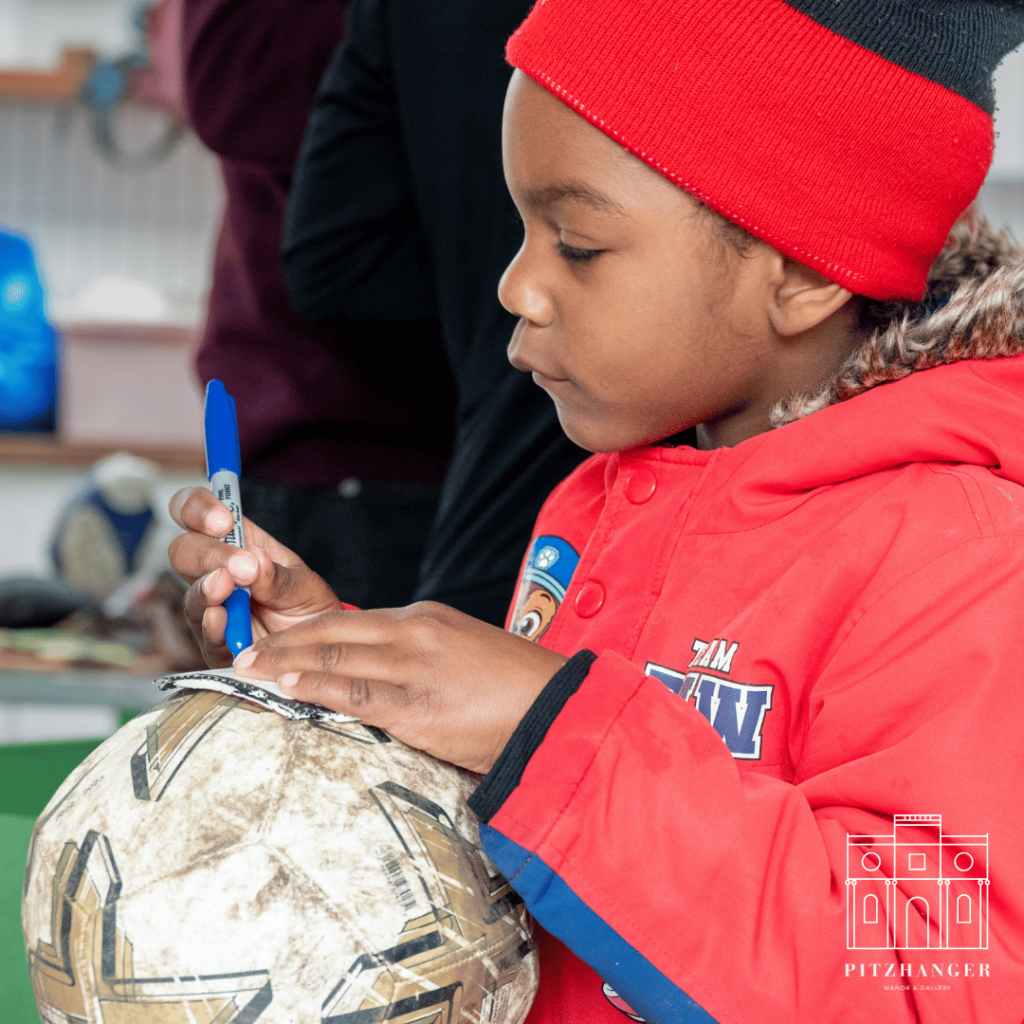 A young child intently decorates a patchwork-style ball with markers during a creative workshop at Pitzhanger Manor.