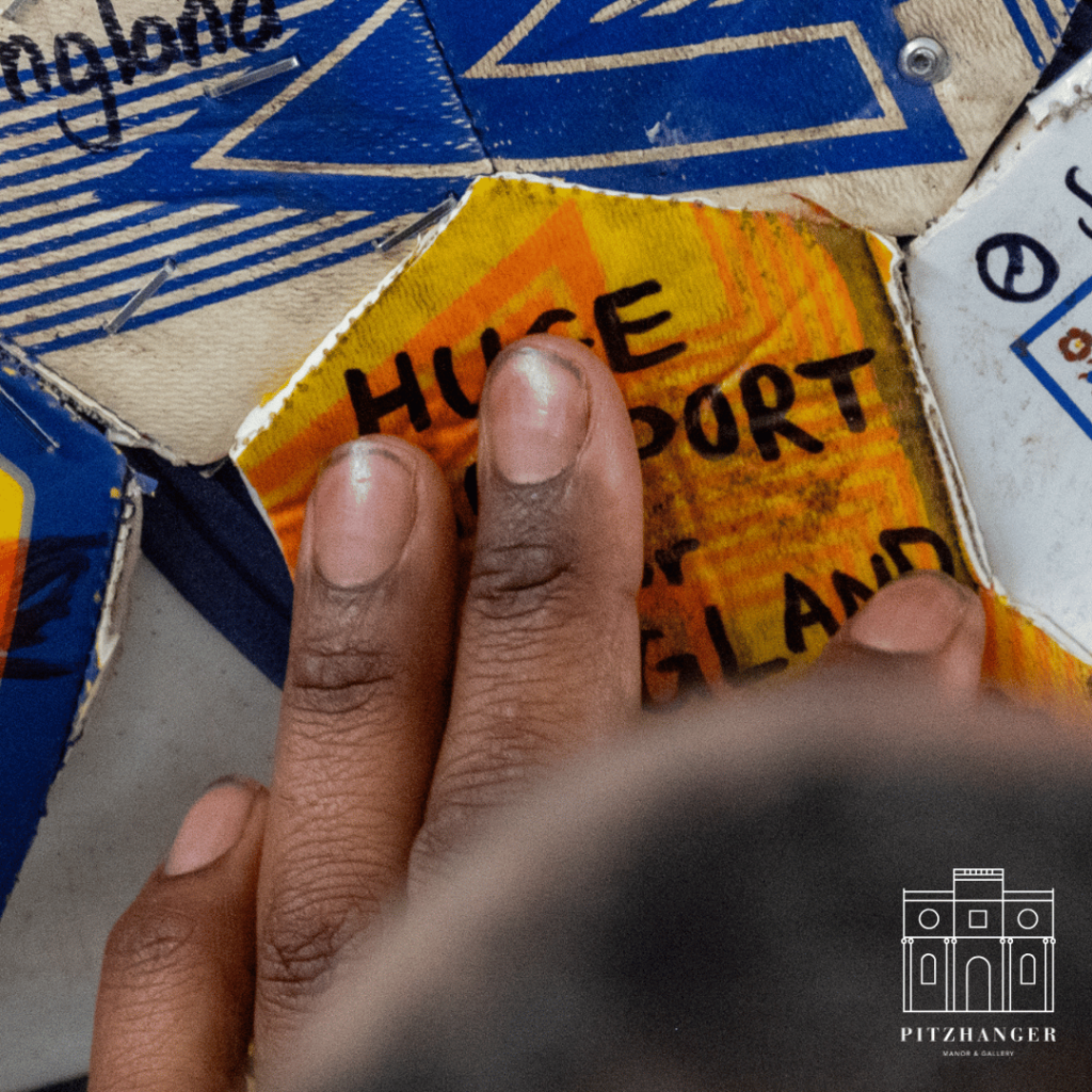 Close-up of a hand pointing to a patch labeled “Huge Support for England” on a collaborative art project.