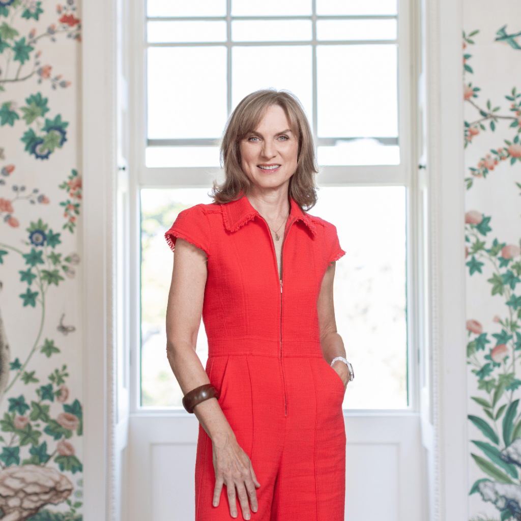 A presenter in a bright red outfit stands against the exquisite interiors of Pitzhanger Manor, embodying sophistication.