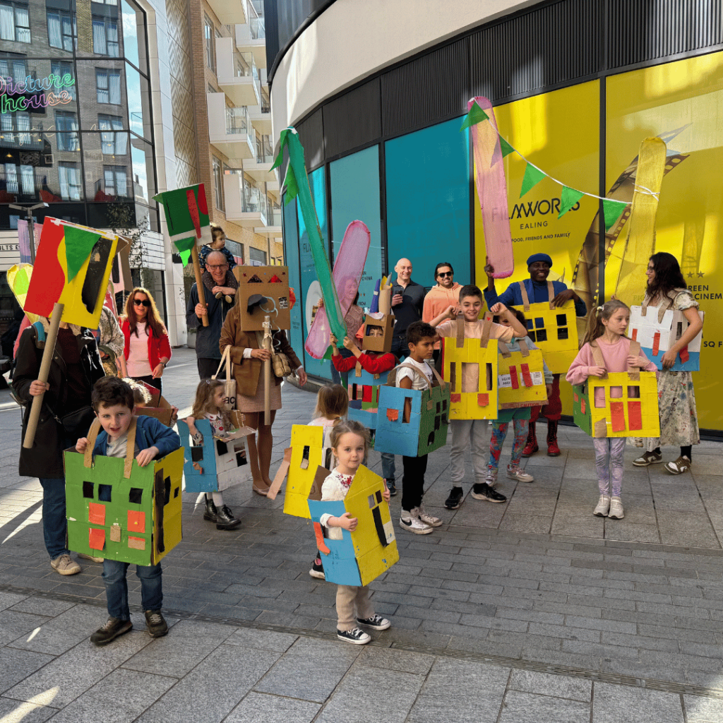 Vibrant procession featuring children wearing colorful cardboard houses, celebrating community creativity and joy.